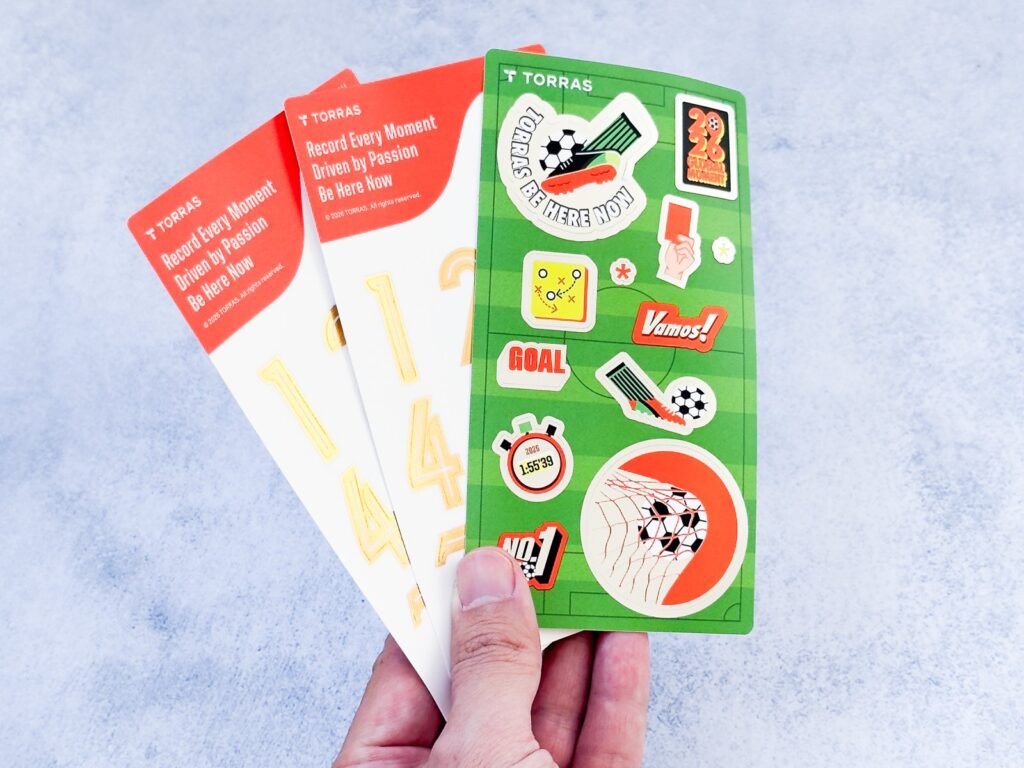 付属のノベルティ。TORRASロゴと「Be Here Now」入りステッカーシートにはサッカー要素のデザインが並ぶ。