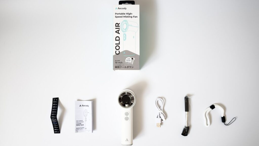 COLD AIRミストファンの付属品一式を俯瞰で並べたもので、上にパッケージ、下段に温度測定シール、取扱説明書、白い本体、USBケーブル、霧吹き用スプレー、白いストラップが横一列に展開されている。