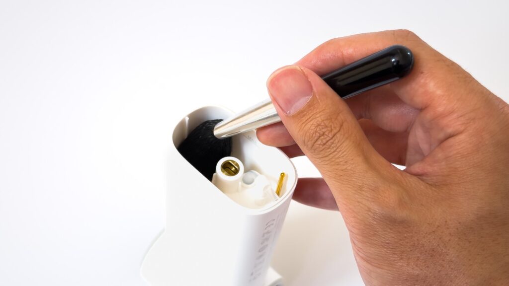 COLD AIRの白いタンク内部を付属の黒い掃除ブラシで清掃している場面。底面には金色の給水接点とプラスチックの突起が見え、開口部からブラシの先端を差し入れている。
