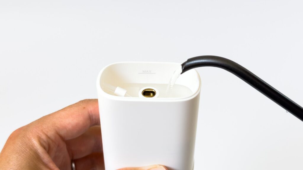 白い給水タンクの開口部に黒い充電ケーブルを差し込んだ状態。内側にMAX水位線と金色の丸い接点、吸水チューブが見え、タンク部から充電する構造を示している。
