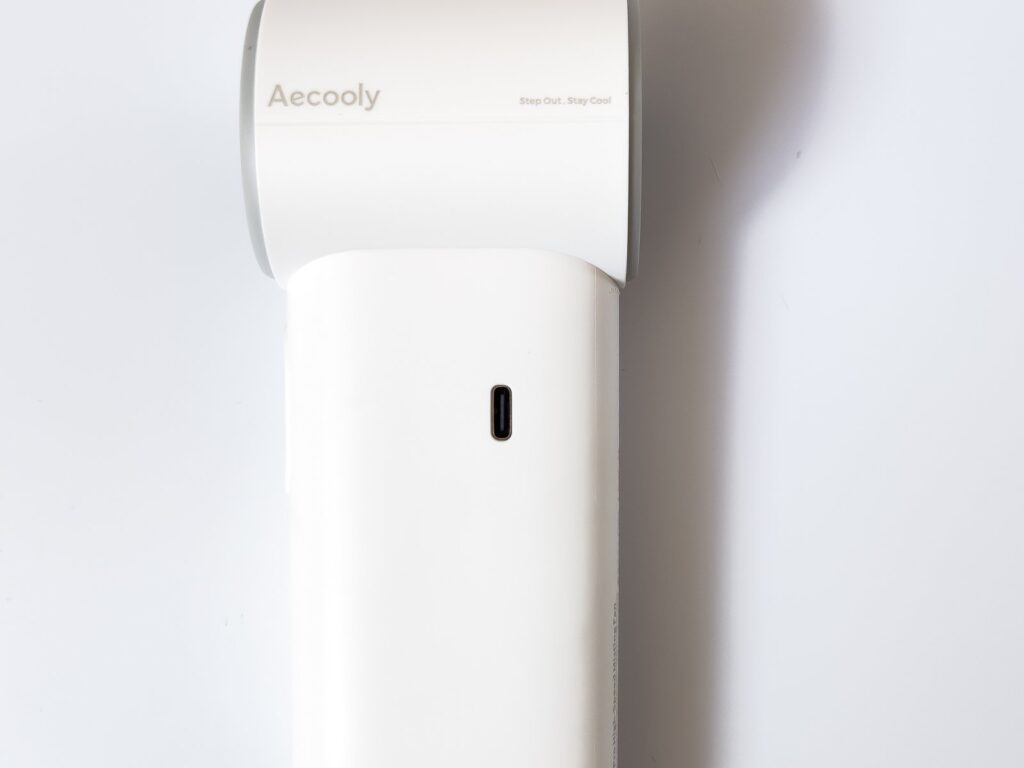 COLD AIR本体側面のAecoolyロゴと「Step Out, Stay Cool」の刻印、その下にある縦長のUSB Type-C充電端子を接写した様子。白い筒型ボディを白背景で正面から捉えている。