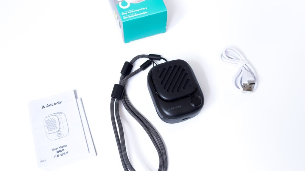 Aecoolyネックファンの付属品一式。白背景に四角い黒の本体、グレーの編み込みストラップ、白いUSB-Cケーブル、Aecoolyロゴ入りのユーザーガイドが並ぶ。本体上面には斜めスリットの吹出口がある。