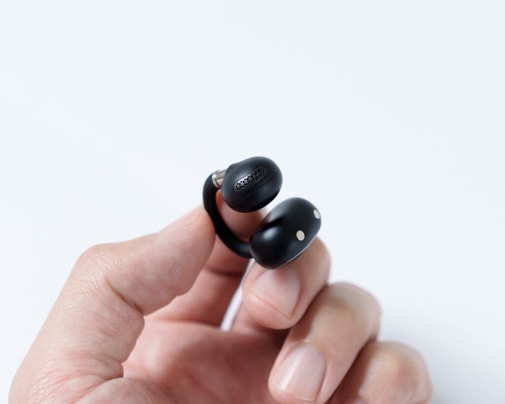 指でつまんだ本体片方。スピーカーのメッシュ部と充電接点を同時に捉えている。