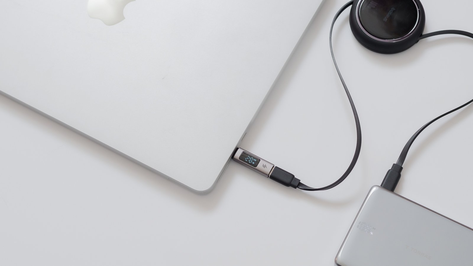 MacBookとモバイルバッテリーをUSB-Cで接続した状態を別角度から捉えたカット。中間のチェッカーに充電中の電力値が表示され、奥に巻き取り式の充電アダプタが置かれている。