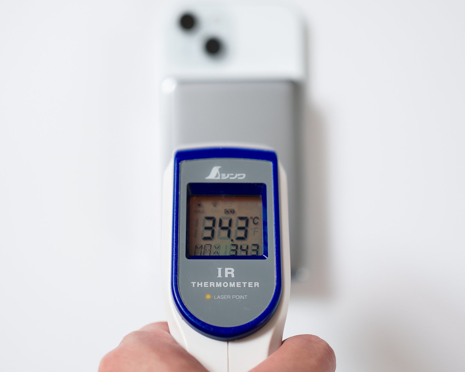 放射温度計でバッテリー表面温度を測定したカット。液晶の表示は34.3℃で、背景にiPhone装着状態のバッテリーが確認できる。