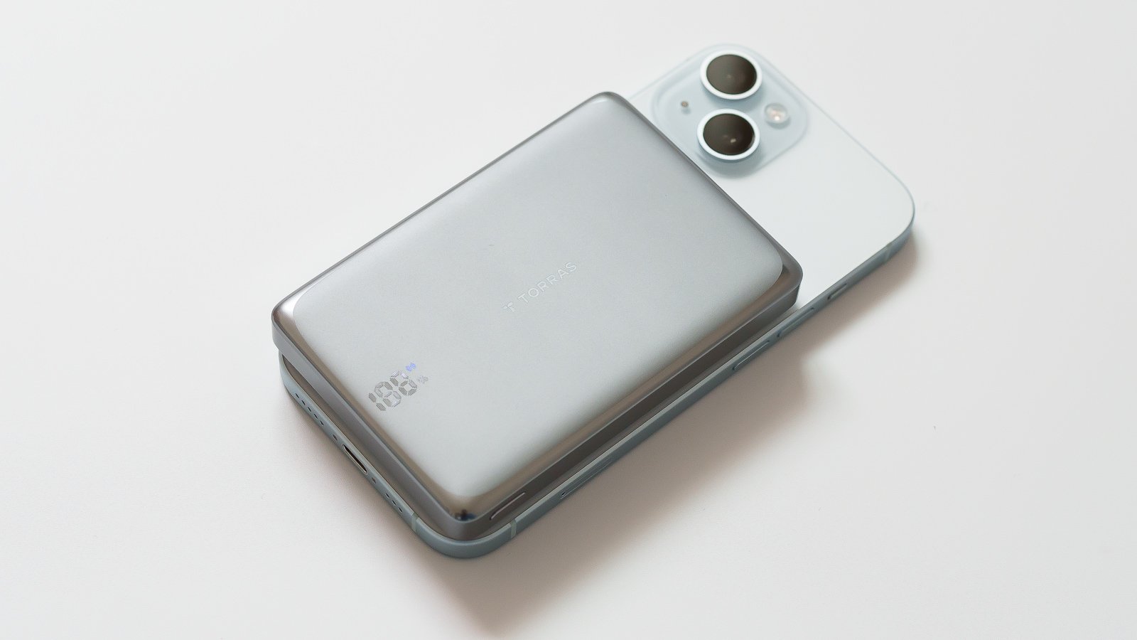 iPhone背面へMagSafeで装着した状態を斜めから撮影。本体下部に残量100%の表示、右上にiPhoneのカメラが見える。