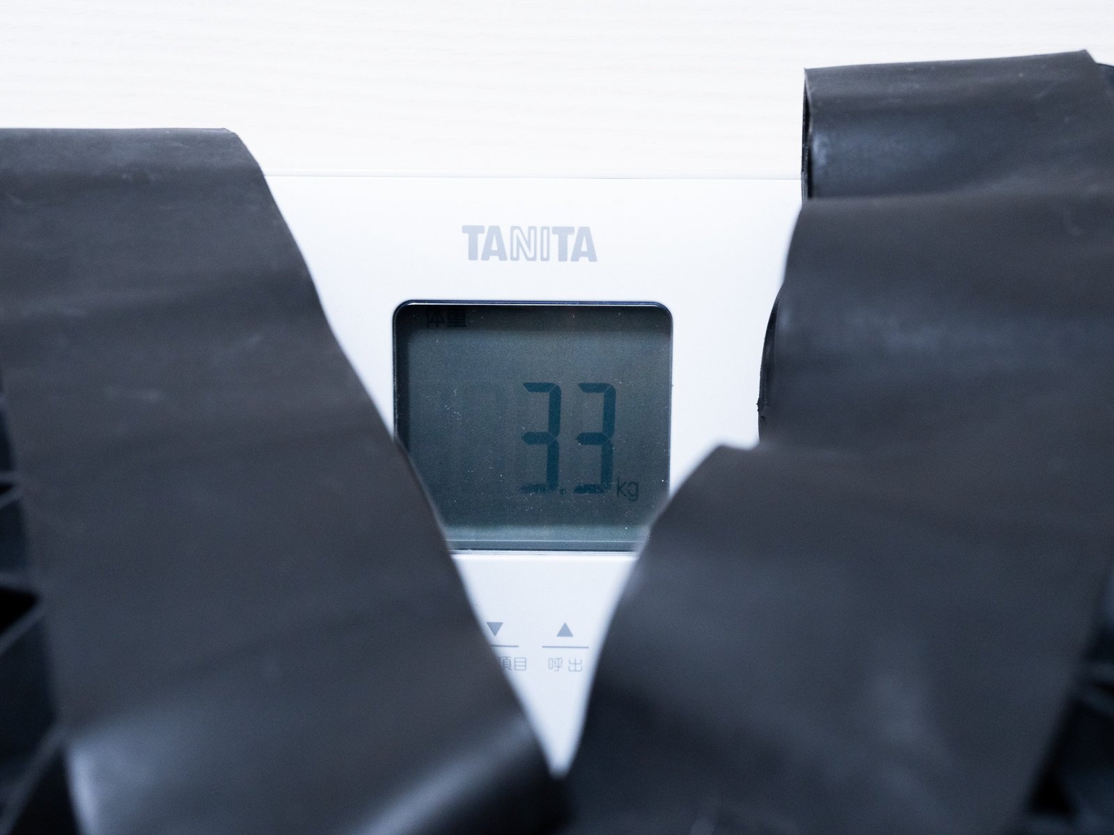 黒い本体を体重計に載せて重量を計測している様子。TANITAの表示部に3.3kgと表示され、本体の間から画面が覗いている。