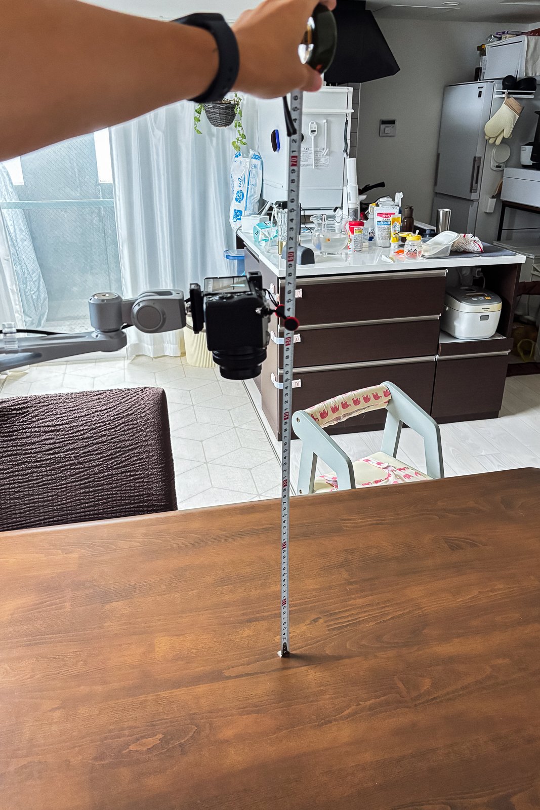 テーブル面からカメラ位置までの高さをコンベックスで測っている手元。カメラはアーム先端で下向きに固定されたままになっている。