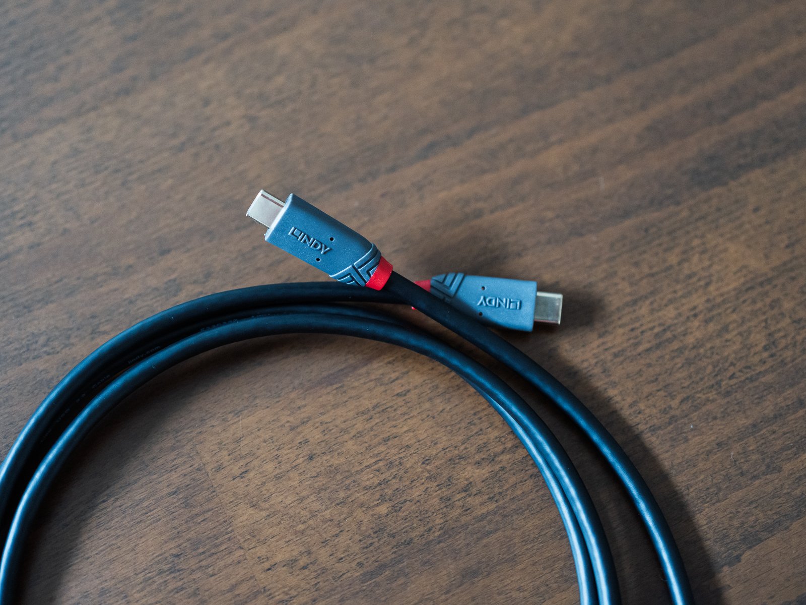 木製テーブルに置いた黒いUSB-Cケーブル。3重に巻かれた状態で両端のコネクタが並び、それぞれ側面にLINDYのロゴが入る。