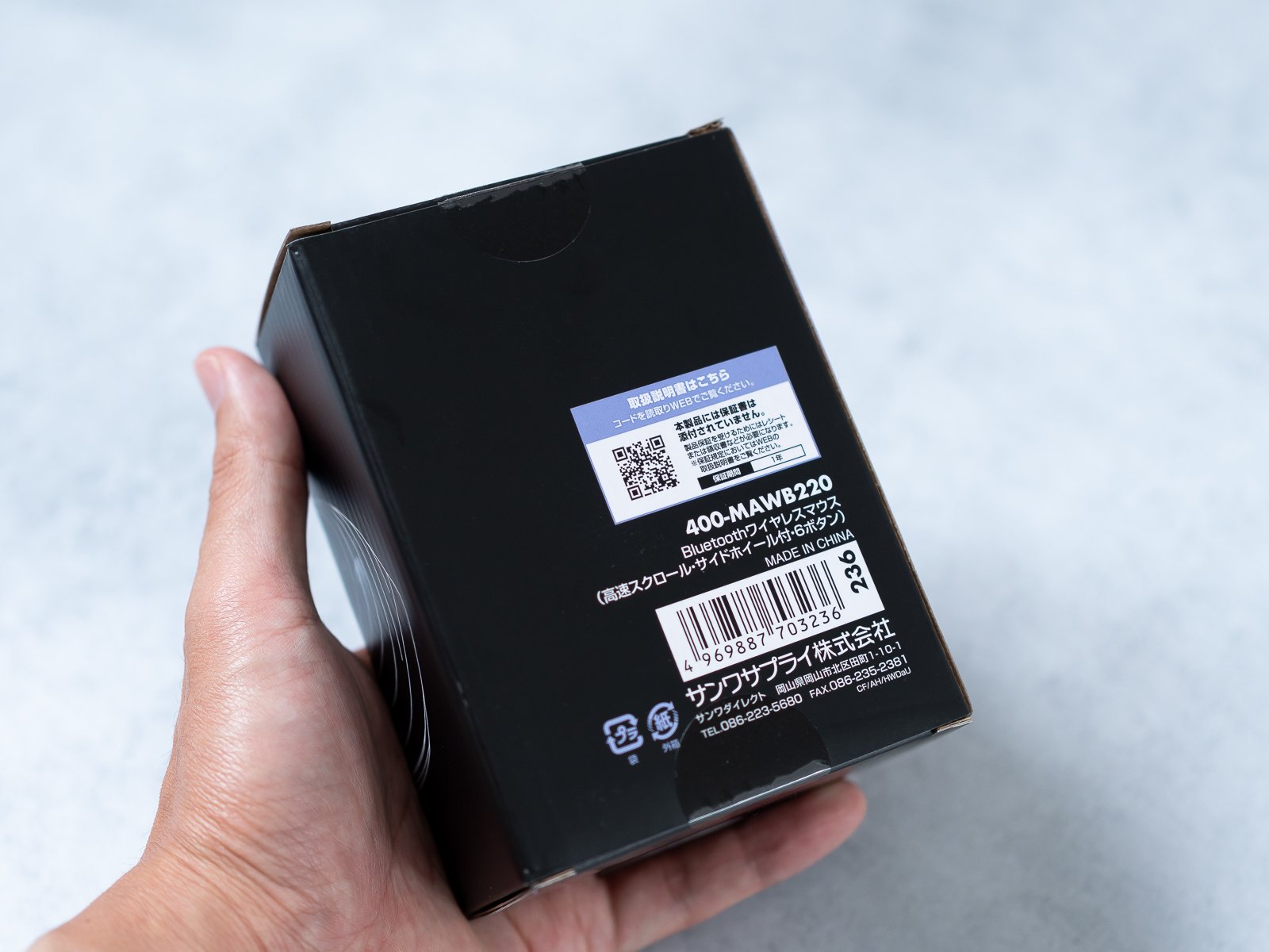 パッケージ裏面を手に持って写したカット。型番400-MAWB220、Bluetoothワイヤレスマウス・高速スクロール・サイドホイール付・6ボタンの表記とバーコードが読み取れる。