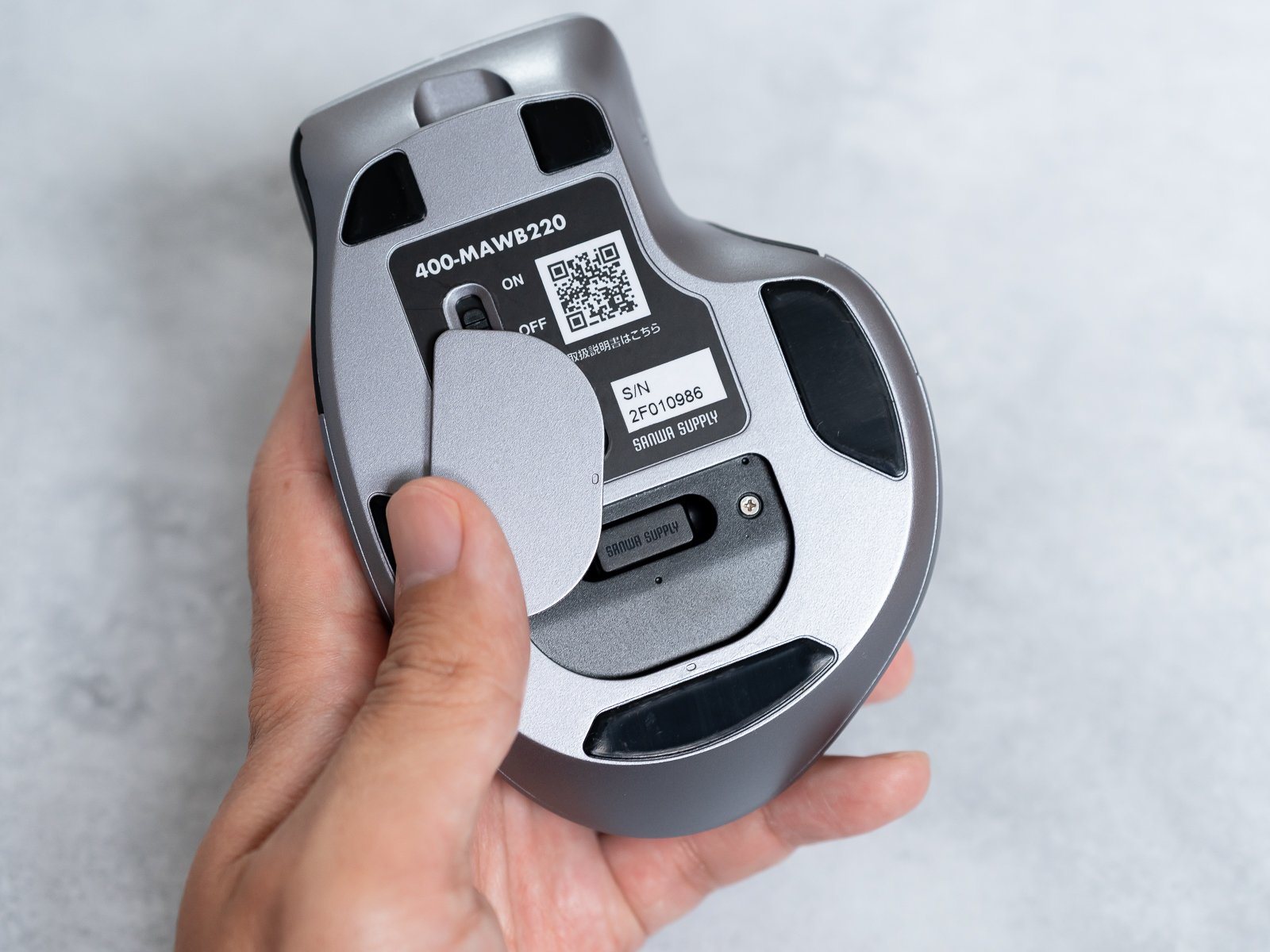 底面のカバーを外して手に持ったカット。型番ラベルと電池・レシーバー収納部、着脱式カバーの磁石が見える。