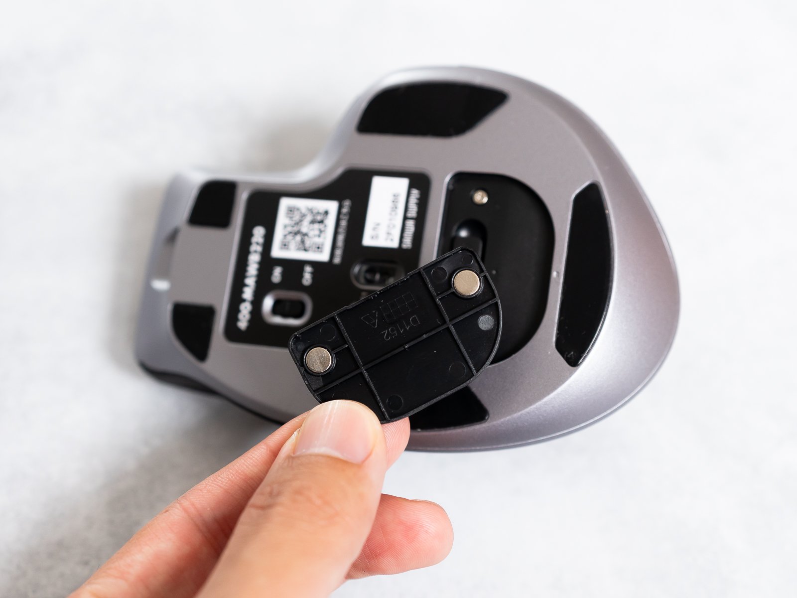 本体底面から取り外した着脱式カバーを指でつまんだカット。裏側に2つの磁石とD1152の刻印がある。