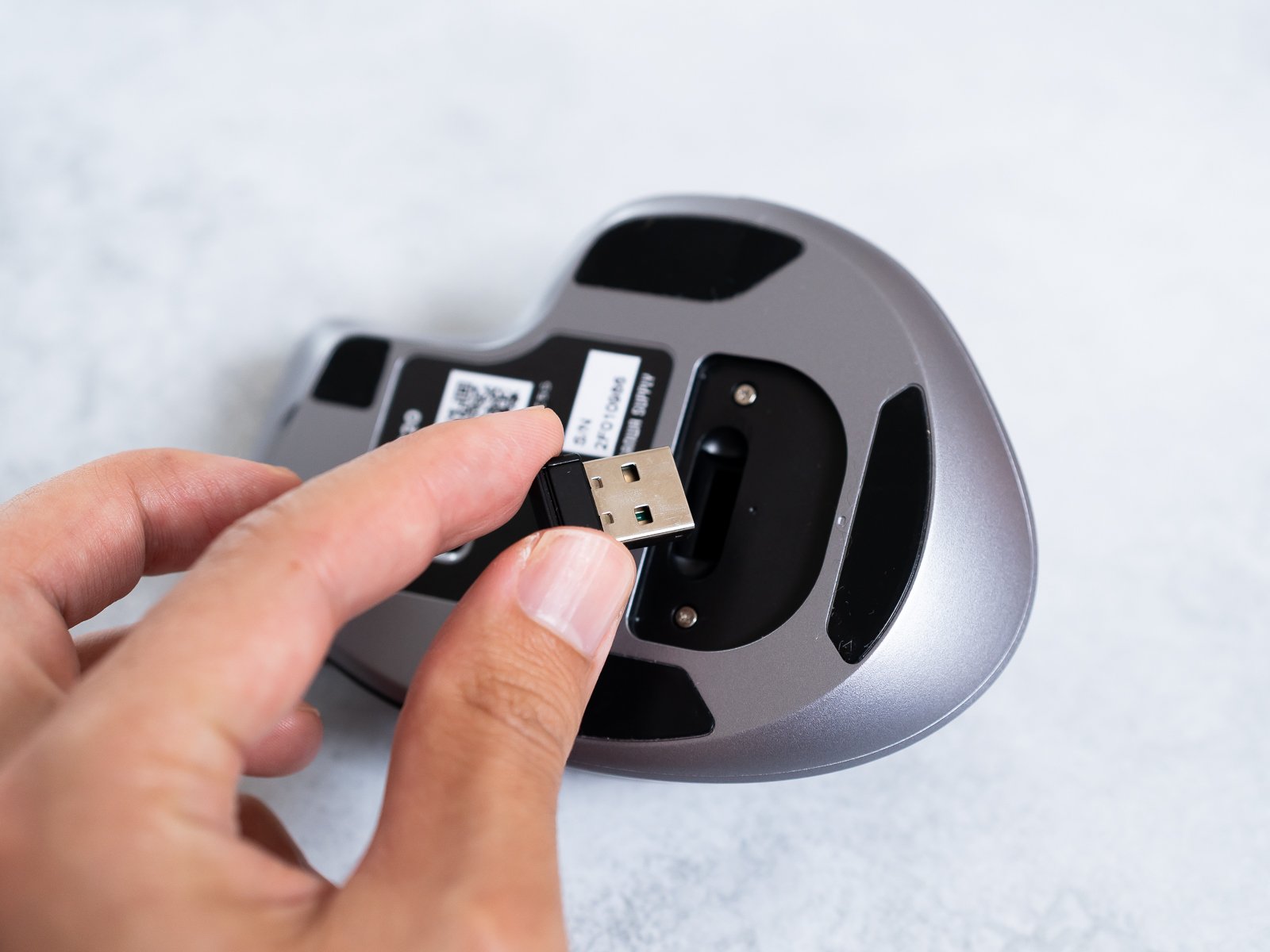 本体底面の収納部からUSBレシーバーを取り出しているカット。無線接続用の小型ドングルが確認できる。