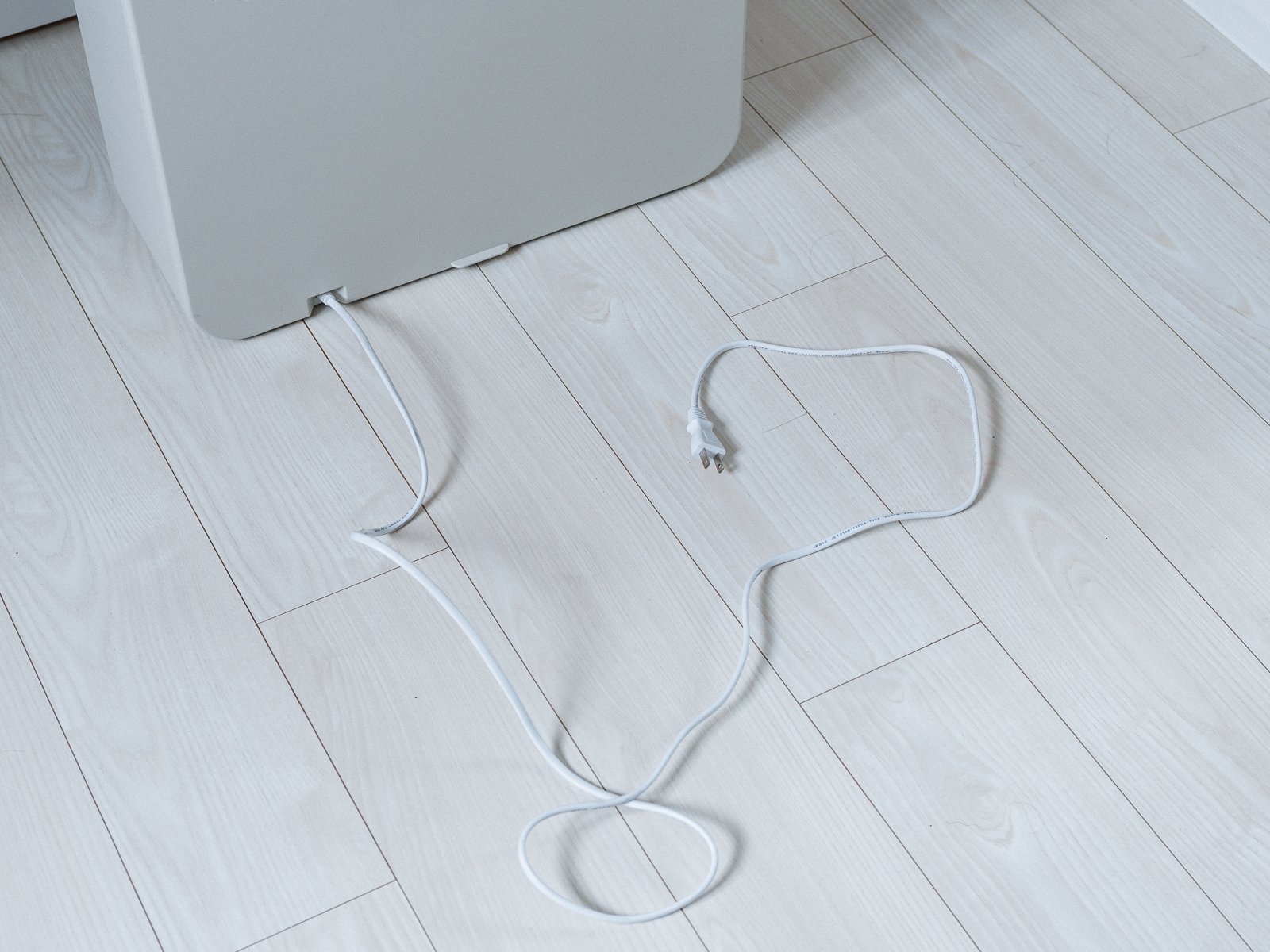 本体下部から伸びる電源コードとプラグを床に広げた状態。フローリングの上でコードの取り回しが確認できる。