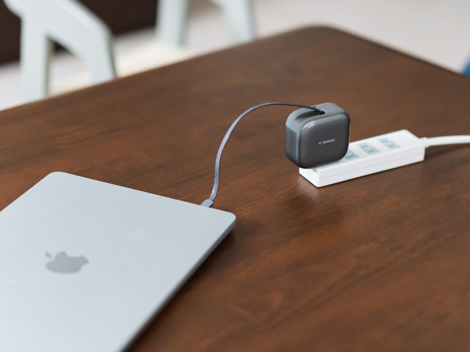 TORRAS FlexLine Pro 60Wを電源タップに差し、内蔵USB-Cケーブルを手前のMacBookへ接続している状態を斜めから捉えている。