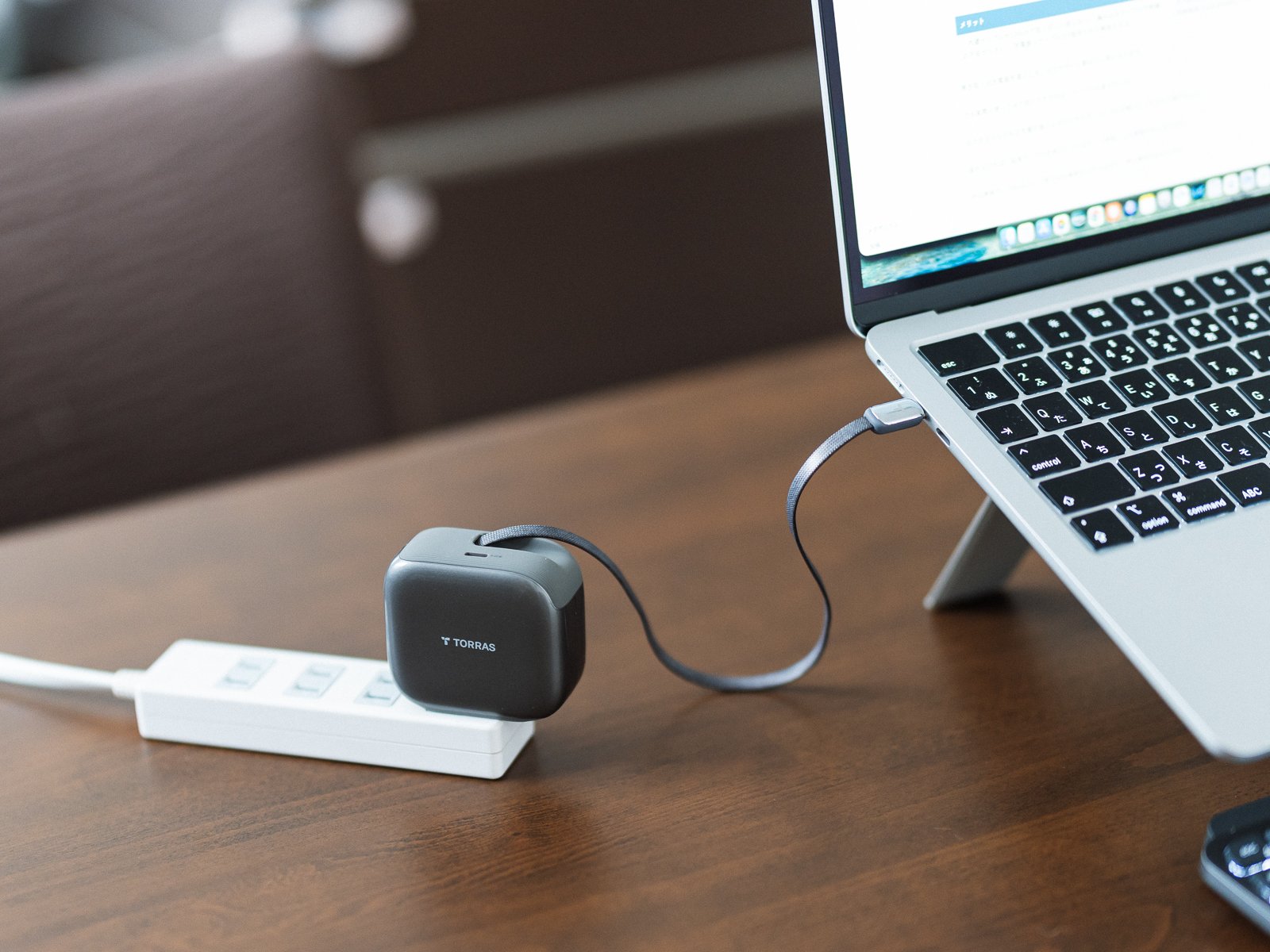 電源タップに差したTORRAS FlexLine Pro 60Wから内蔵ケーブルを伸ばし、スタンド上のMacBookを充電している状態。