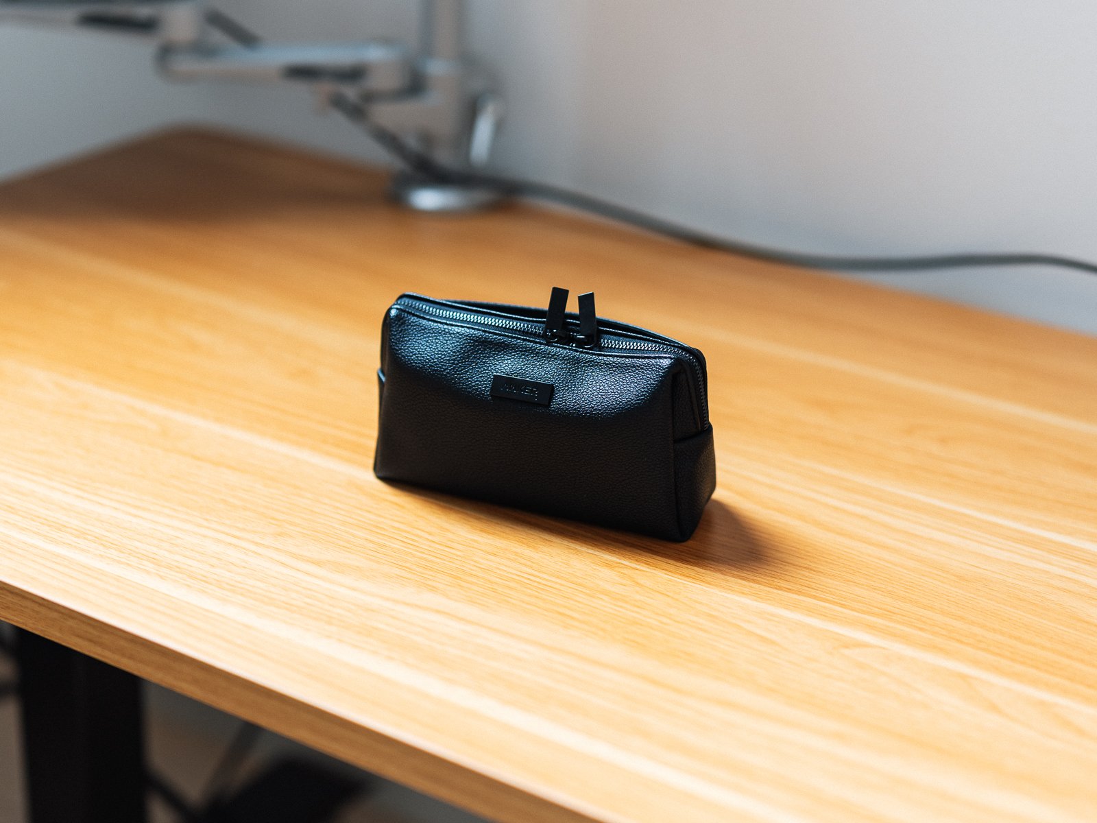木目のデスク上に自立させたAnker Style Pouch。黒い本体の厚みと側面のマチ、上部のダブルファスナーが確認できる。