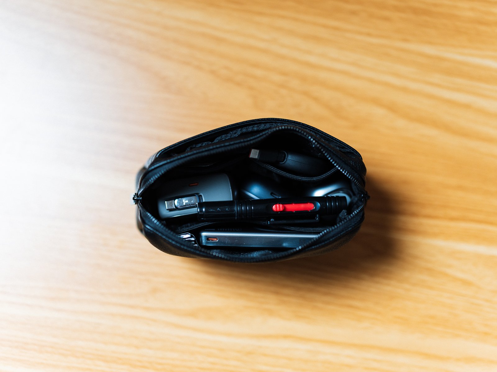 Anker Style Pouchのファスナーを開き、複数のガジェットを収納した状態。充電器や清掃用品が内部に収まっている。