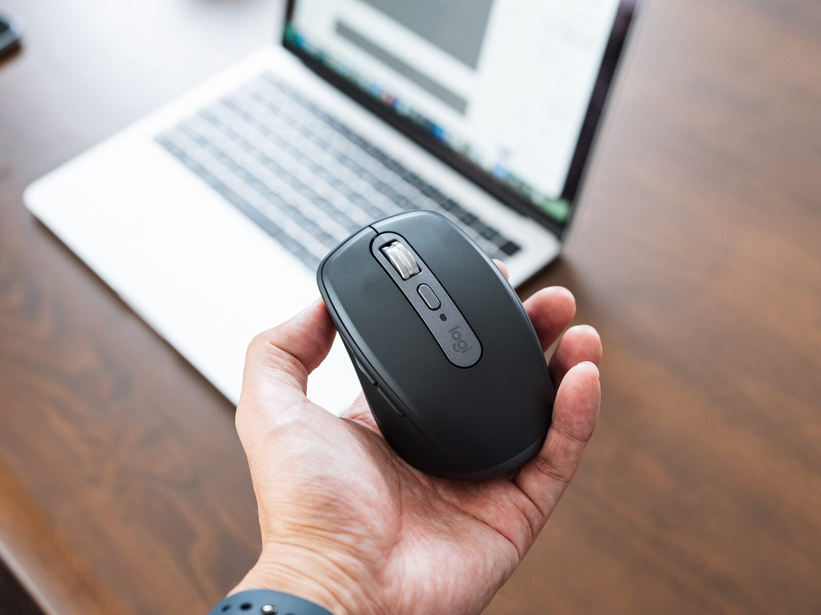 ロジクールのマウスMX Anywhere 3Sを手のひらに載せた状態。背景に開いたノートPCがある。
