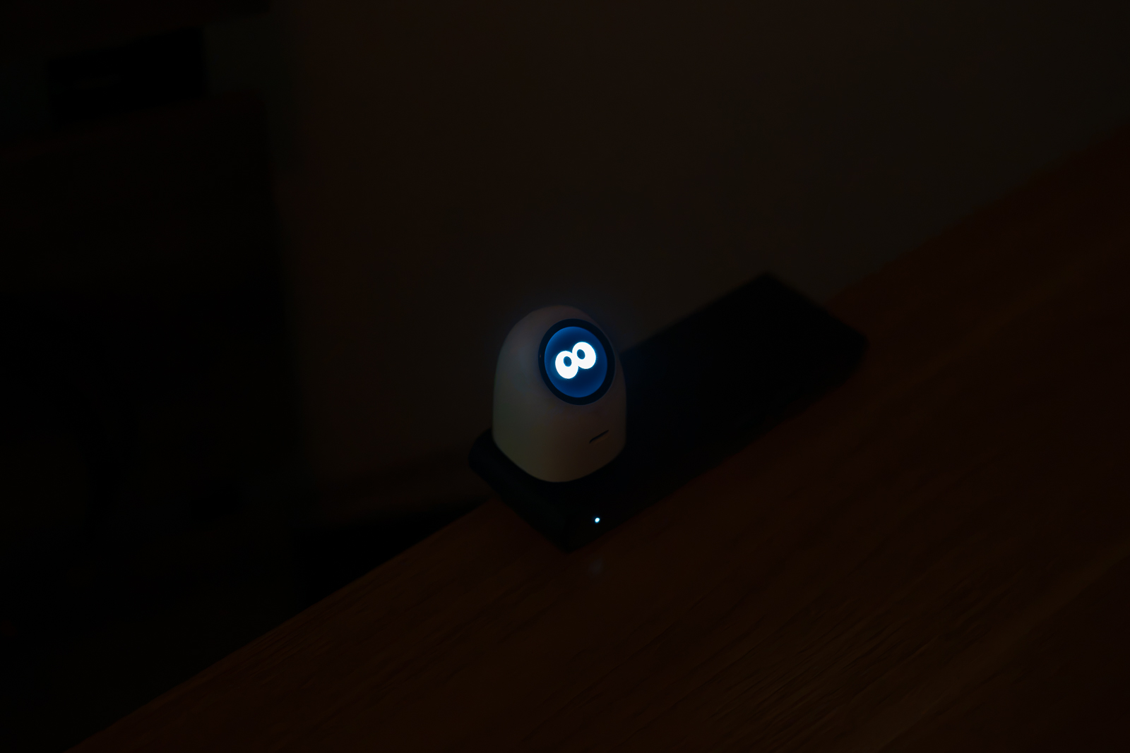 暗い部屋で電源タップに挿したTORRAS FlashEye Dot。黒い画面に青白い目の表情だけが浮かび、周囲はほとんど照らされていない。