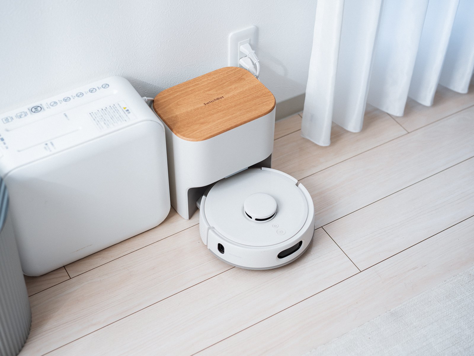 SwitchBot ロボット掃除機 K11+ Proとゴミ収集ステーションを上から見たカット。白い円形の本体がステーションに収まり、木目調のフタにロゴが入っている。