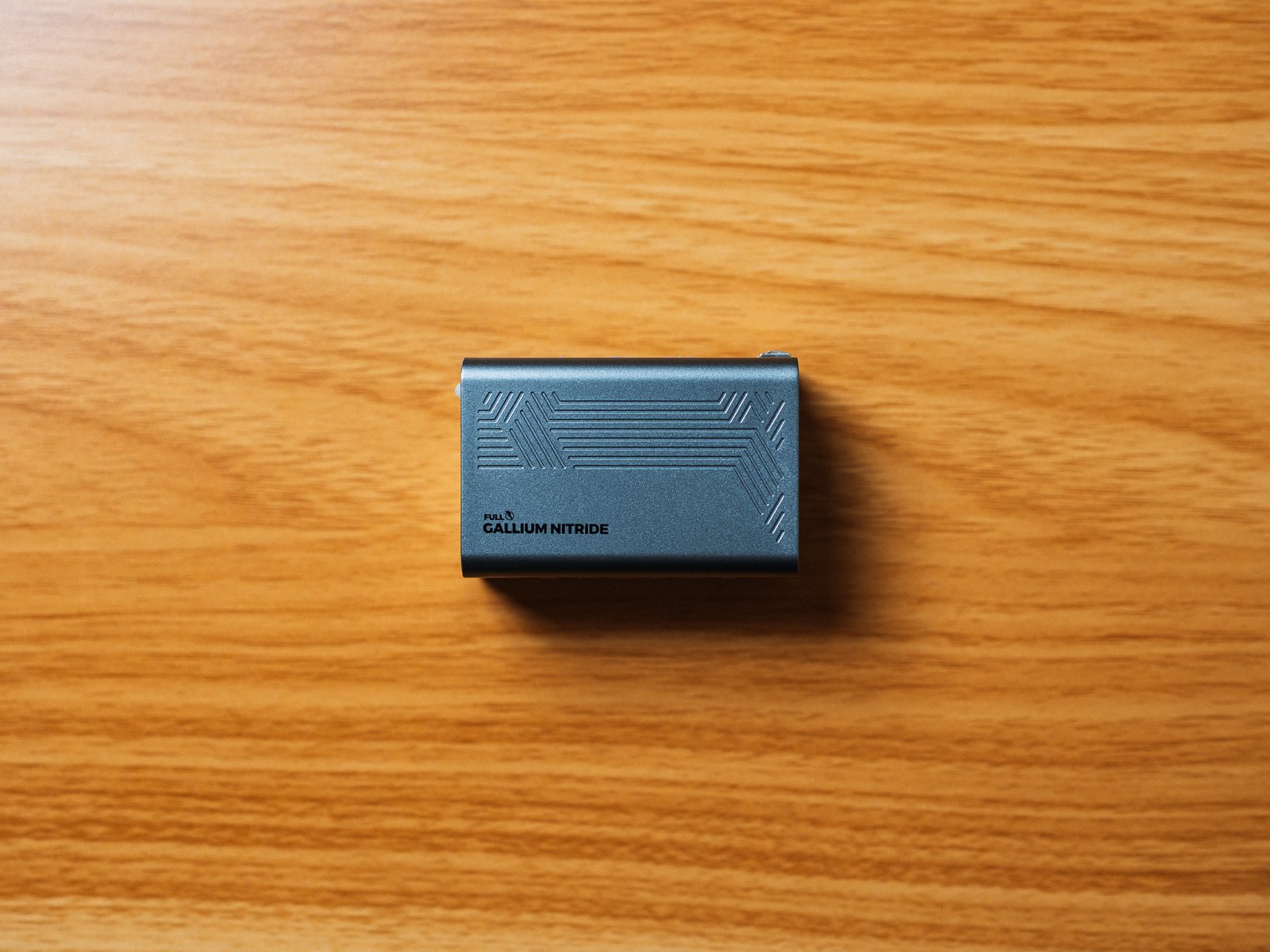 木目のデスクに横向きに置いたPHYSCE 67W GaN急速充電器のウェッブグレー。側面に直線的な溝の模様とGALLIUM NITRIDEの文字が入っている。