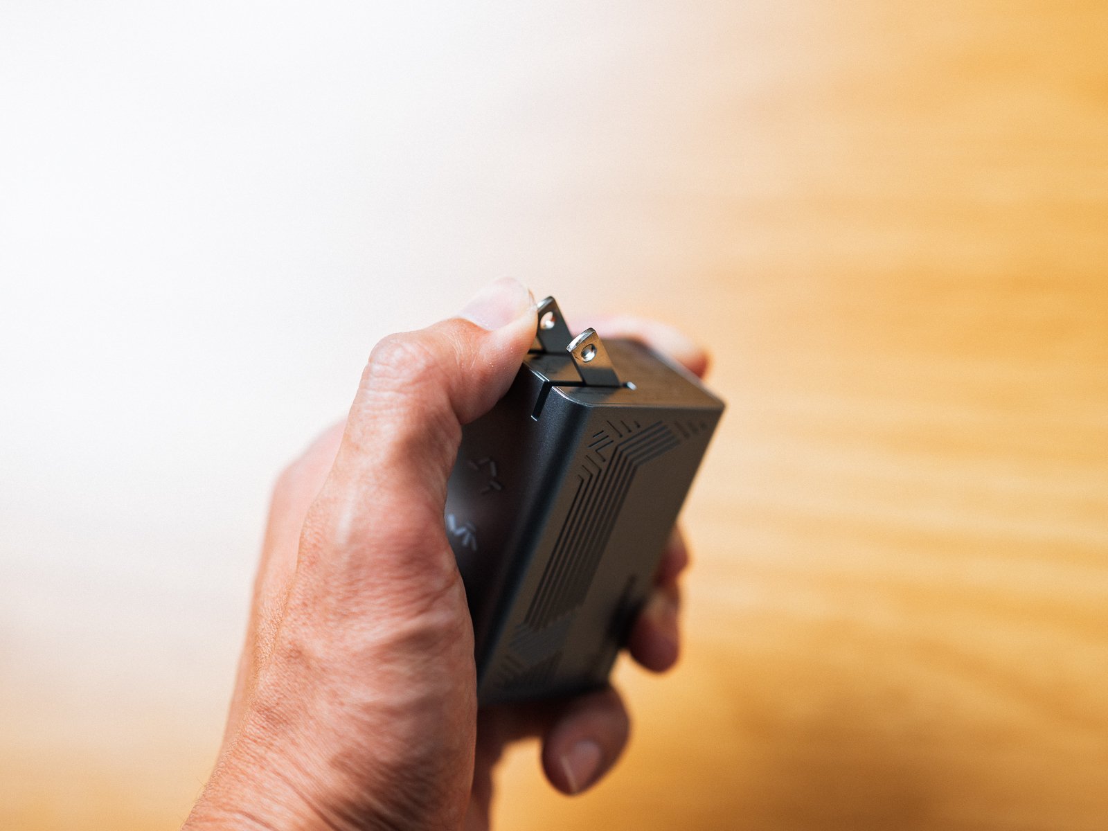 折りたたみ式のプラグを起こした状態で手に持ったPHYSCE 67W GaN急速充電器。本体の端から金属のプラグが2本出ている。