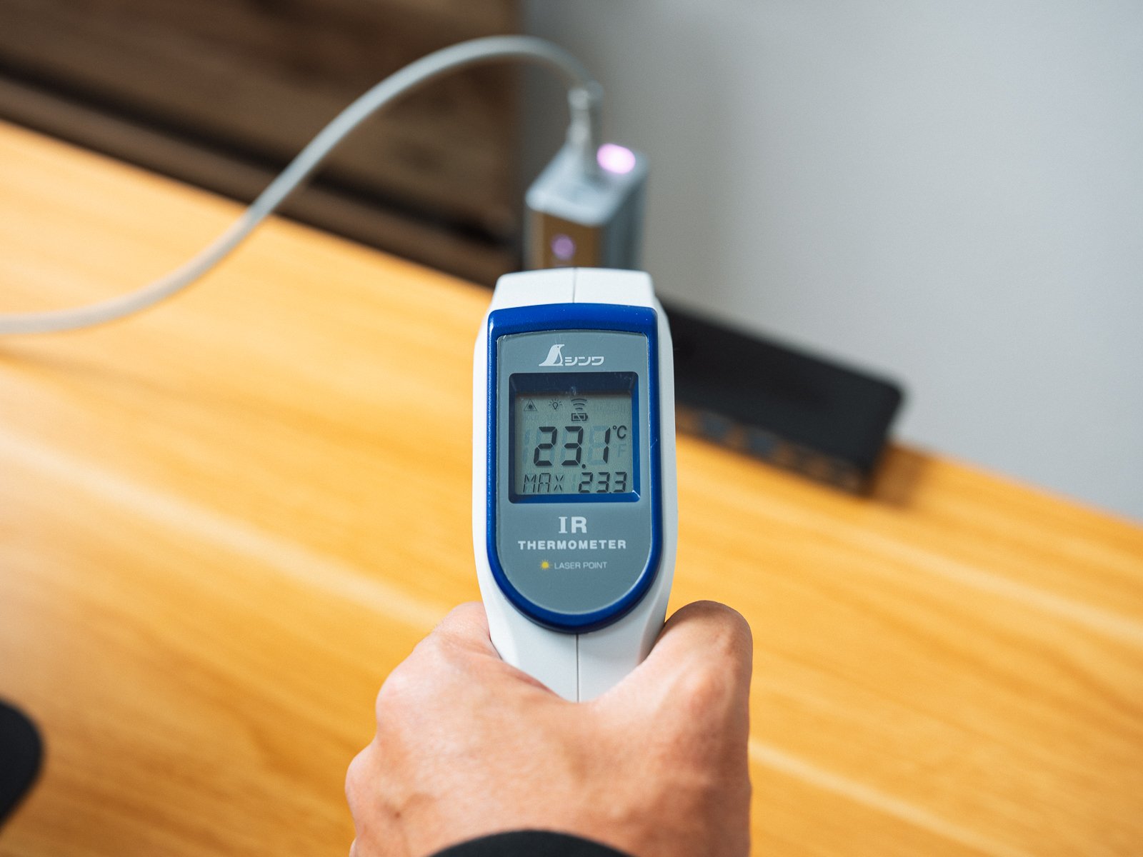 赤外線温度計でPHYSCE 67W GaN急速充電器の表面温度を測っている様子。充電を始めた時点の表示は23.1℃を示している。