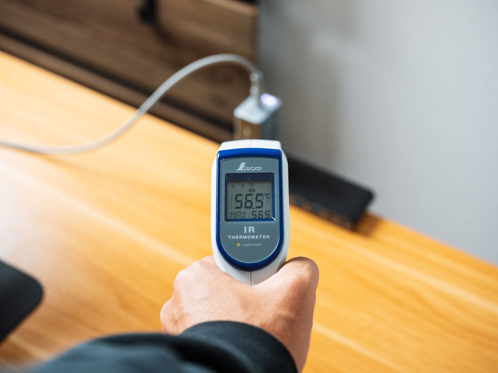 赤外線温度計でPHYSCE 67W GaN急速充電器の表面温度を測っている様子。30分充電したあとの表示は56.5℃を示している。