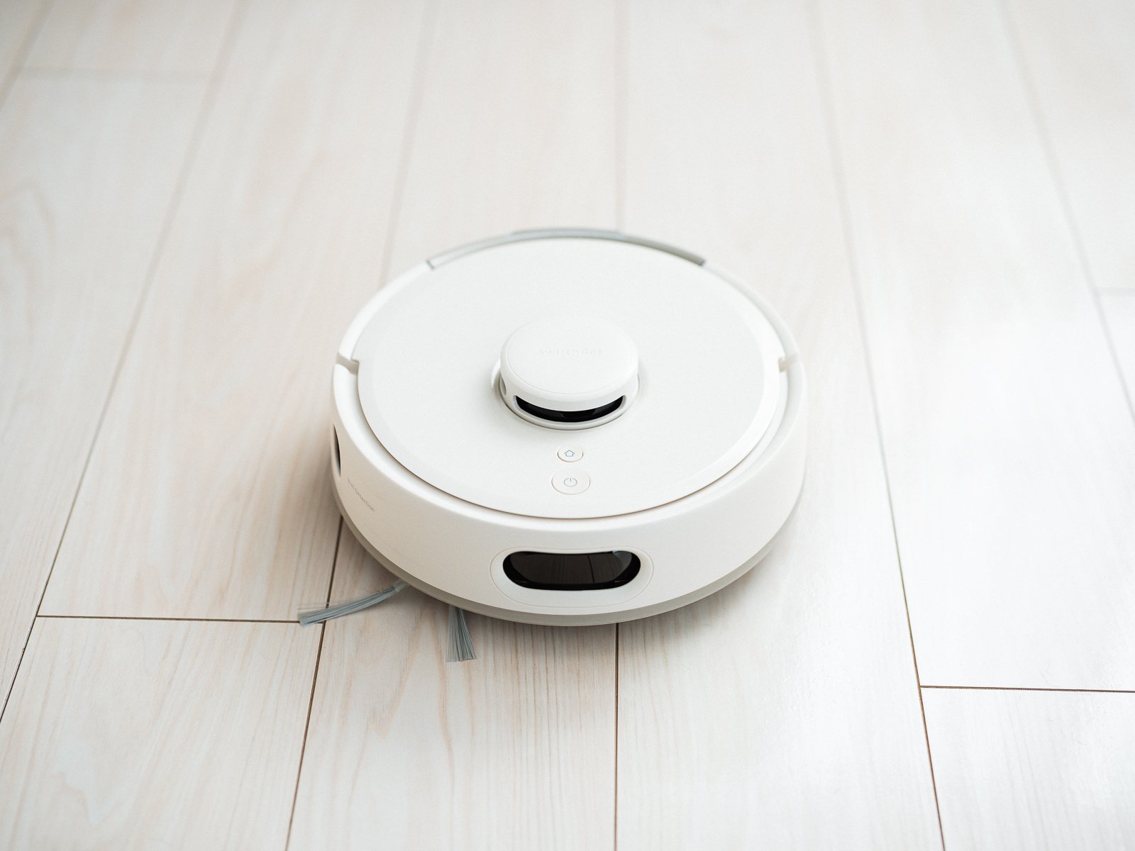 フローリングに置いたSwitchBot K11+ Proを斜め前から見たところ。前面に横長のセンサー窓、天面にレーザーセンサー