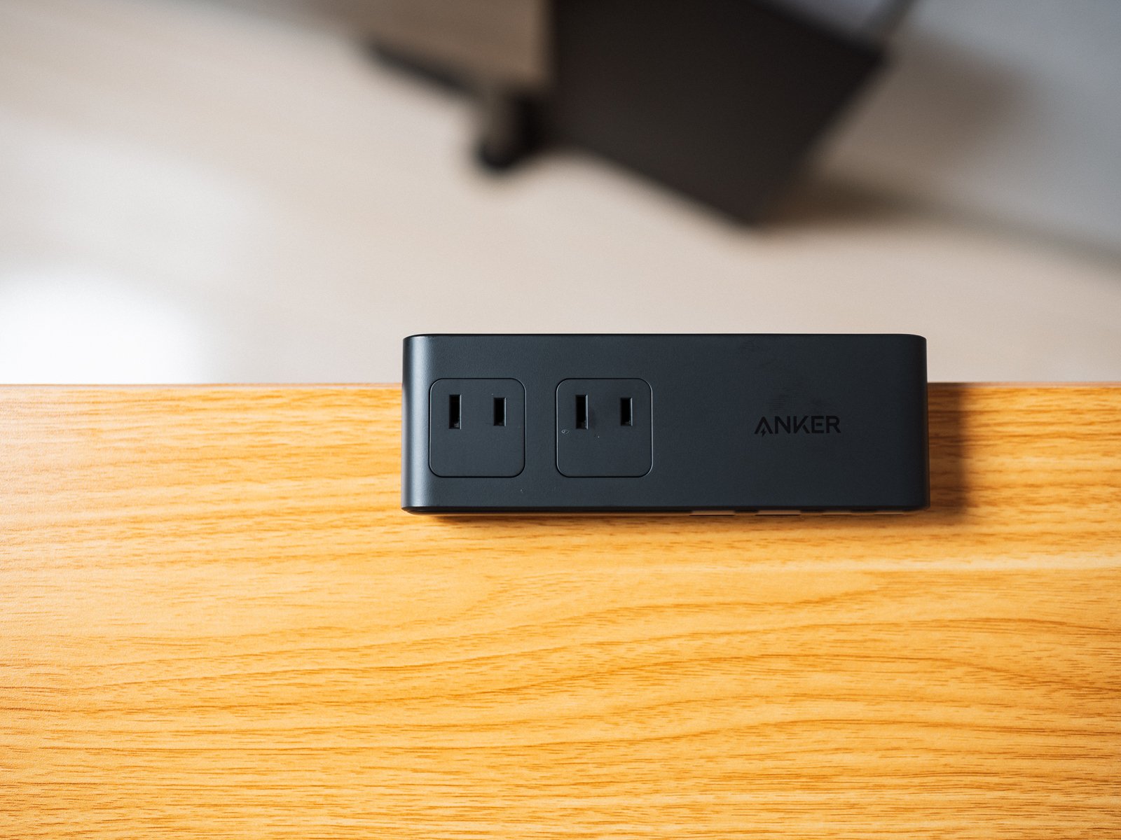 木製デスクの端に置いた黒い電源タップを正面から捉えた様子。上面にコンセントの差込口が2つ並び、差込口どうしの間隔が分かる。
